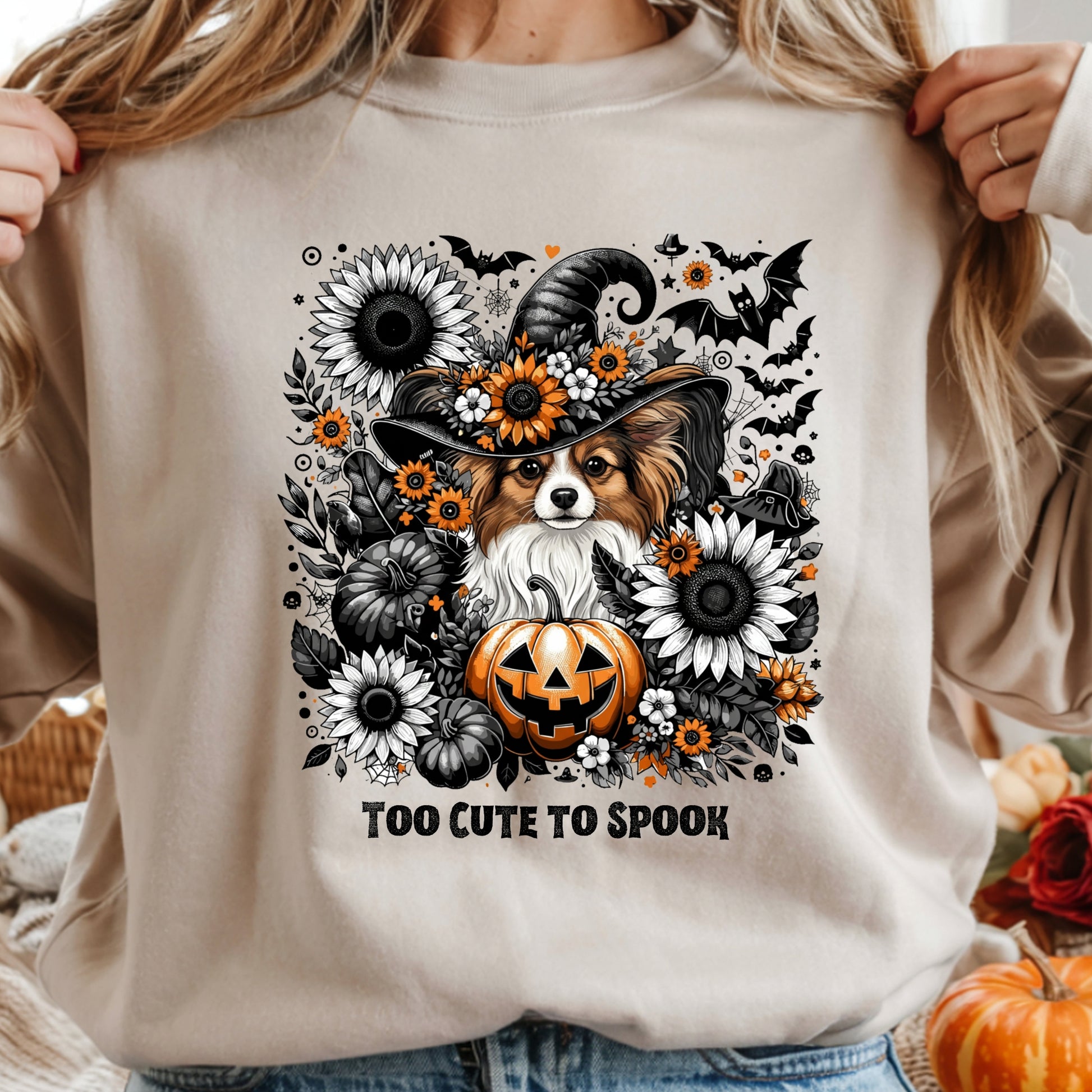 Beige sweatshirt with a Halloween-themed design featuring a dog in a witch hat, pumpkins, and flowers.