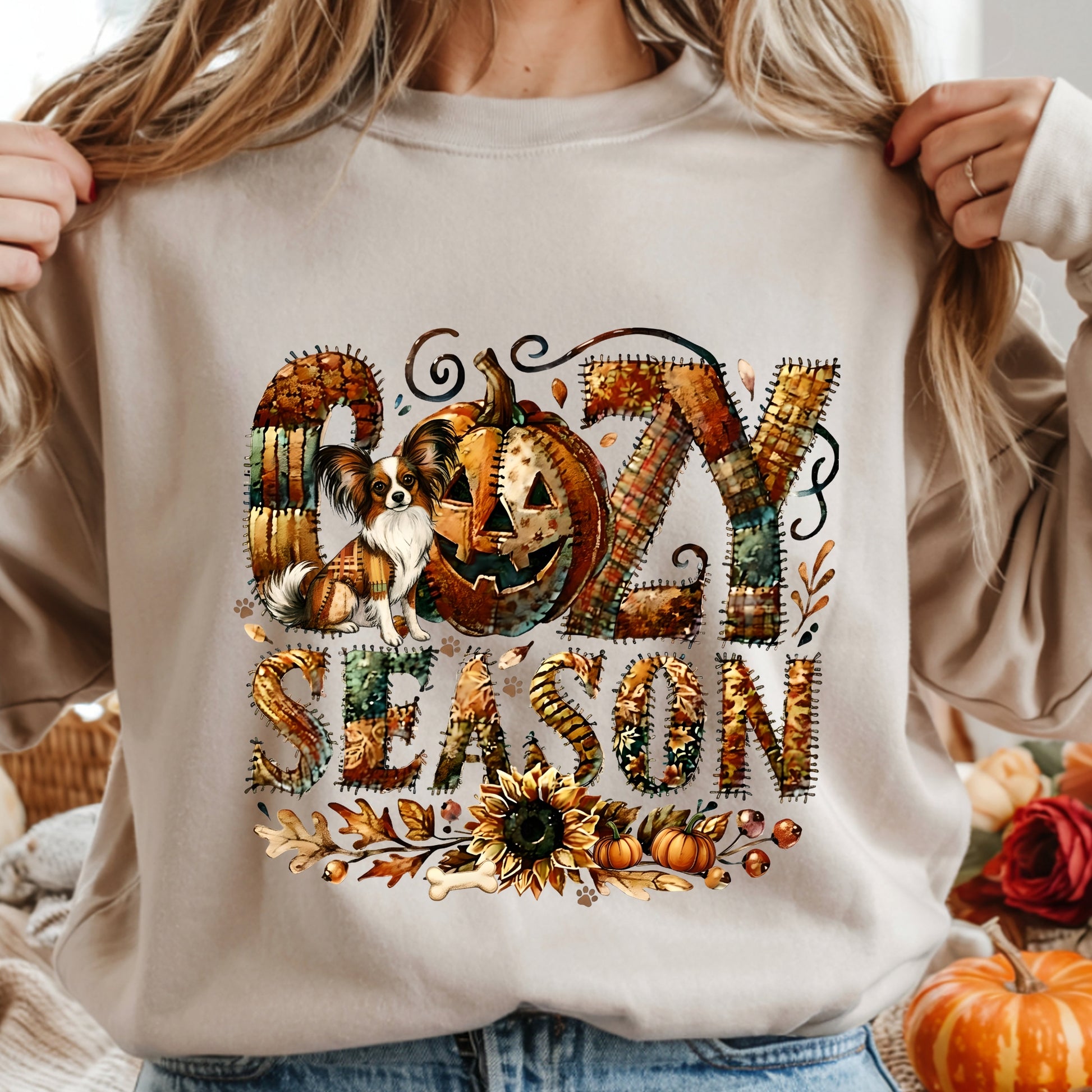 Beige sweatshirt with 'Gozy Season' design featuring pumpkins and a dog, held by a person.