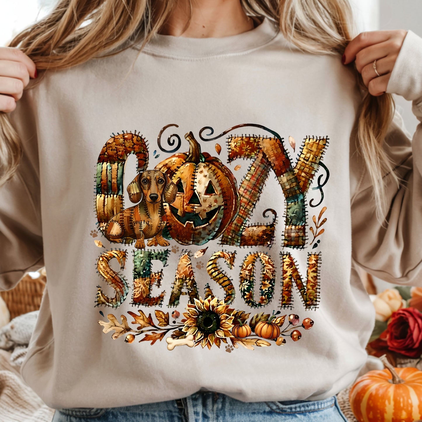 Cozy Season patchwork sweatshirt featuring a hidden Dachshound in autumn colors, surrounded by pumpkins, leaves, and a sunflower.Cozy patchwork sweatshirt with "Cozy Season" text, autumn colors, pumpkins, sunflower, and a hidden Dachshound motif.
