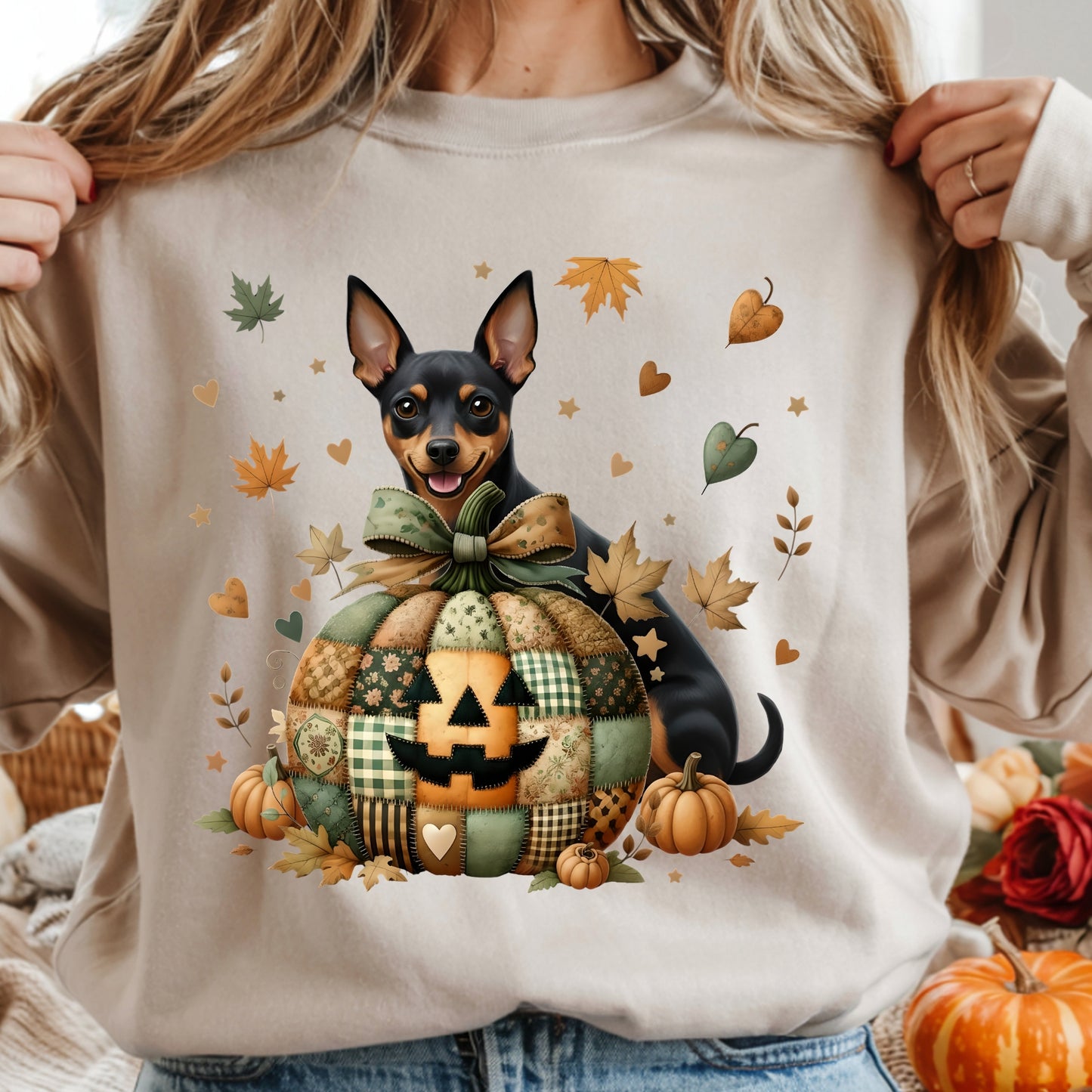 Person wearing a beige sweatshirt with a dog and pumpkin design, surrounded by autumn leaves and pumpkins.
