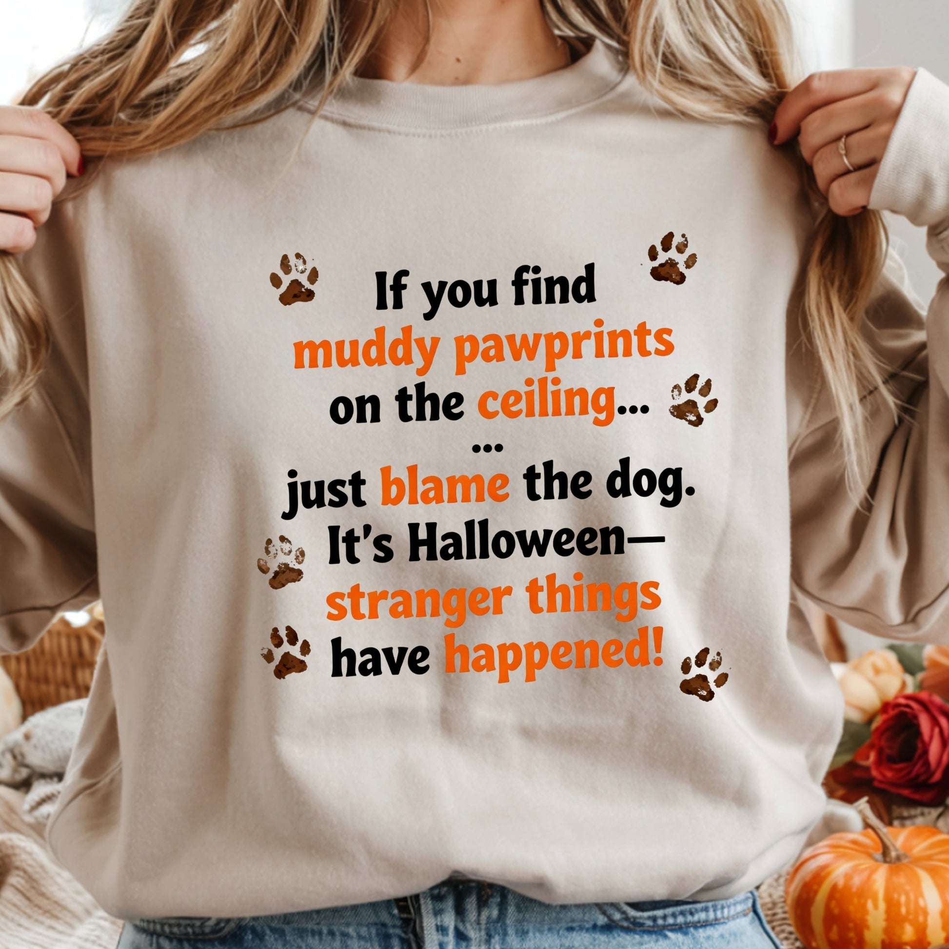 Person wearing a beige sweatshirt with Halloween-themed text and paw prints.