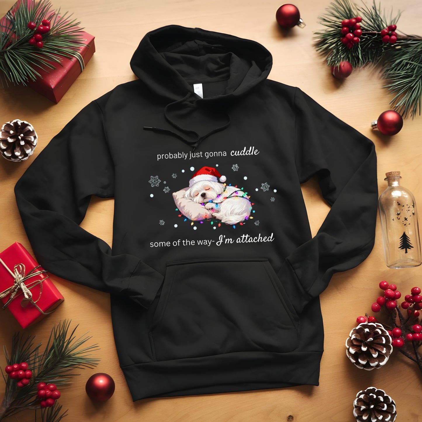 Black hoodie with Christmas-themed design on a wooden surface with holiday decorations.