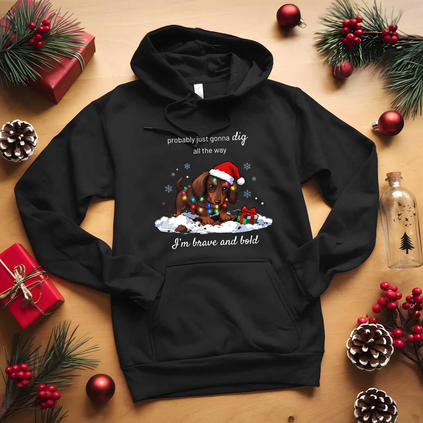 Black hoodie with Christmas-themed design on a wooden surface with holiday decorations.