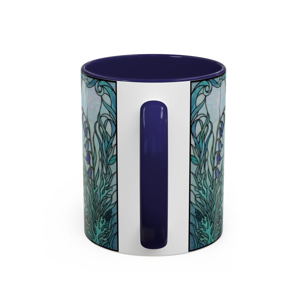 A ceramic mug with a deep navy blue handle and interior, featuring a white vertical band and teal and blue stained-glass style floral patterns on the sides, shown on a white background.