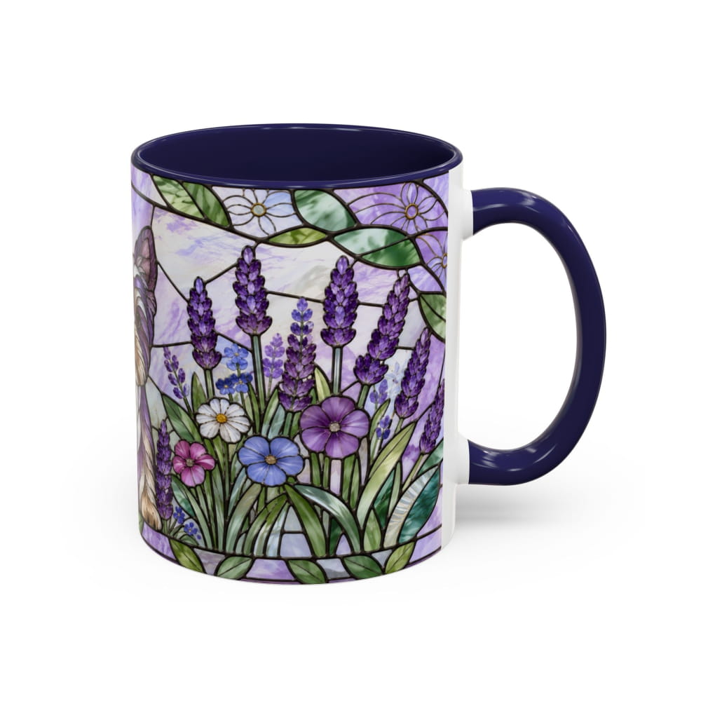 A ceramic mug with a dark navy blue handle and interior, featuring a colorful stained-glass style floral design on the exterior with purple flowers, green leaves, and light background panels.