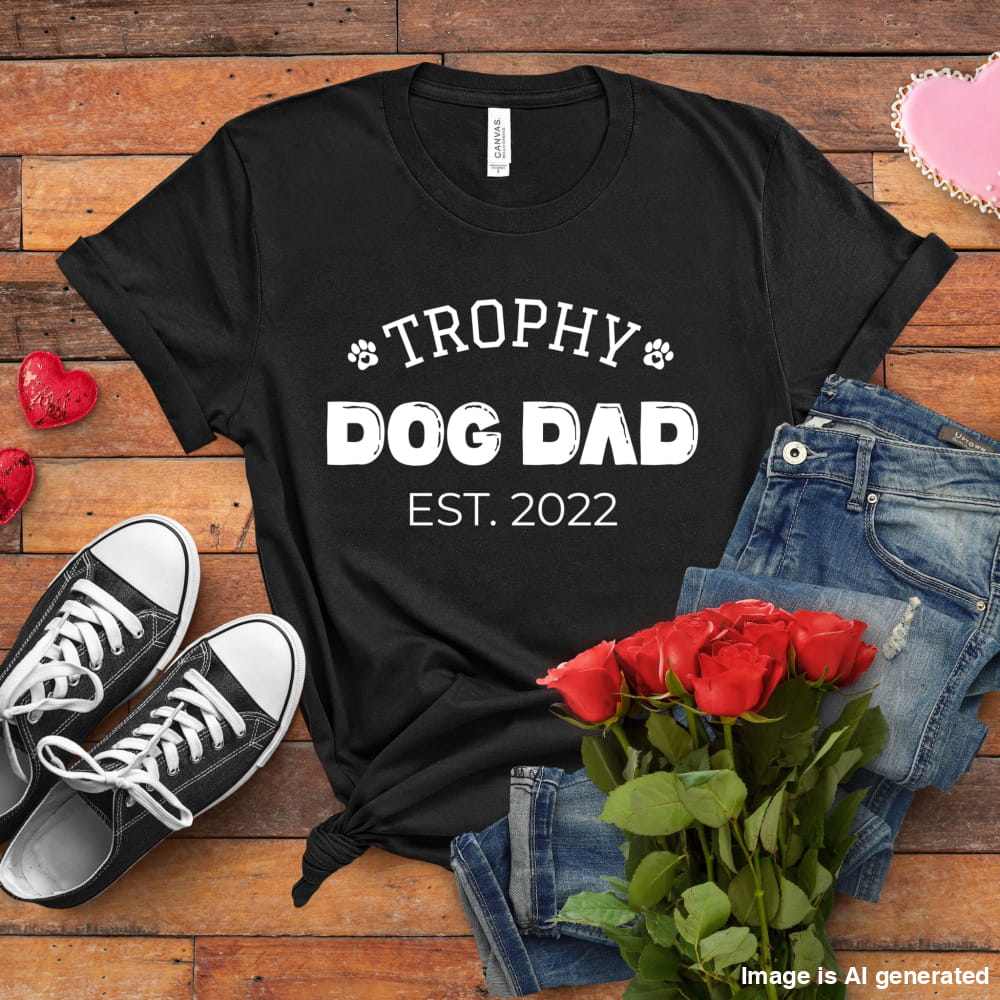 Black t-shirt with 'Trophy Dog Dad Est. 2022' text on a wooden surface with shoes, jeans, and roses.