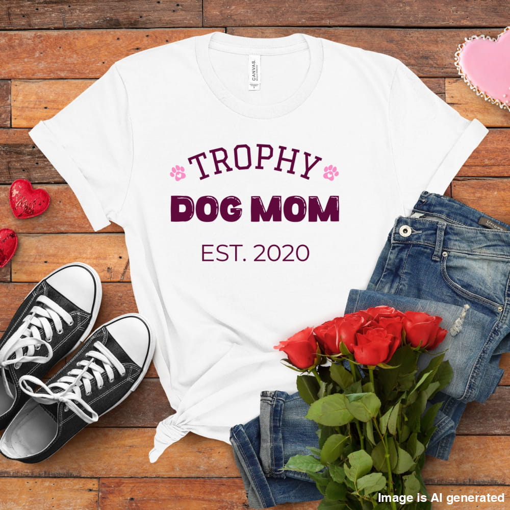 White t-shirt with 'Trophy Dog Mom Est. 2020' text, black sneakers, red roses, and jeans on a wooden surface.