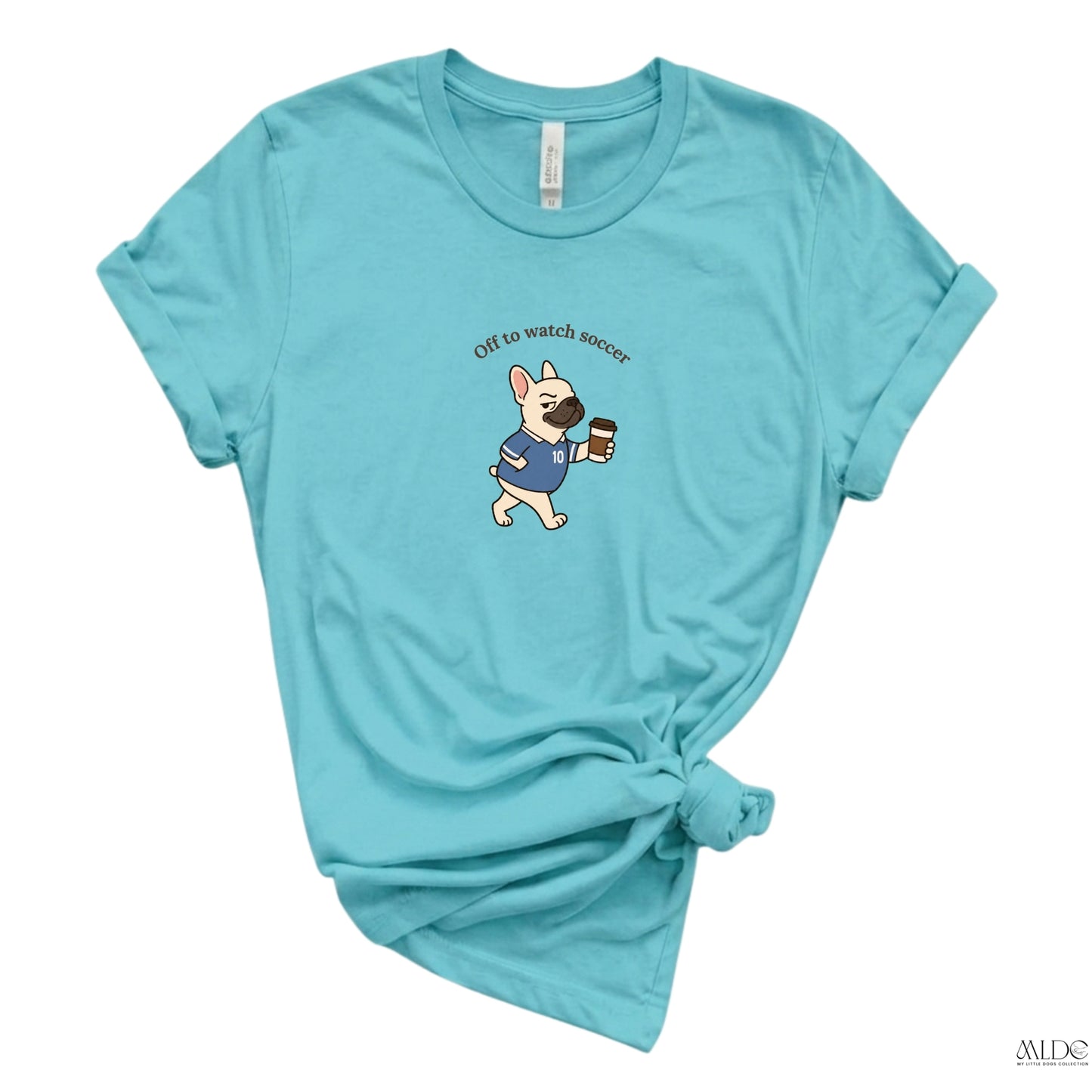 Light blue t-shirt with a cartoon dog holding a coffee cup and text 'Off to watch soccer' on a white background.