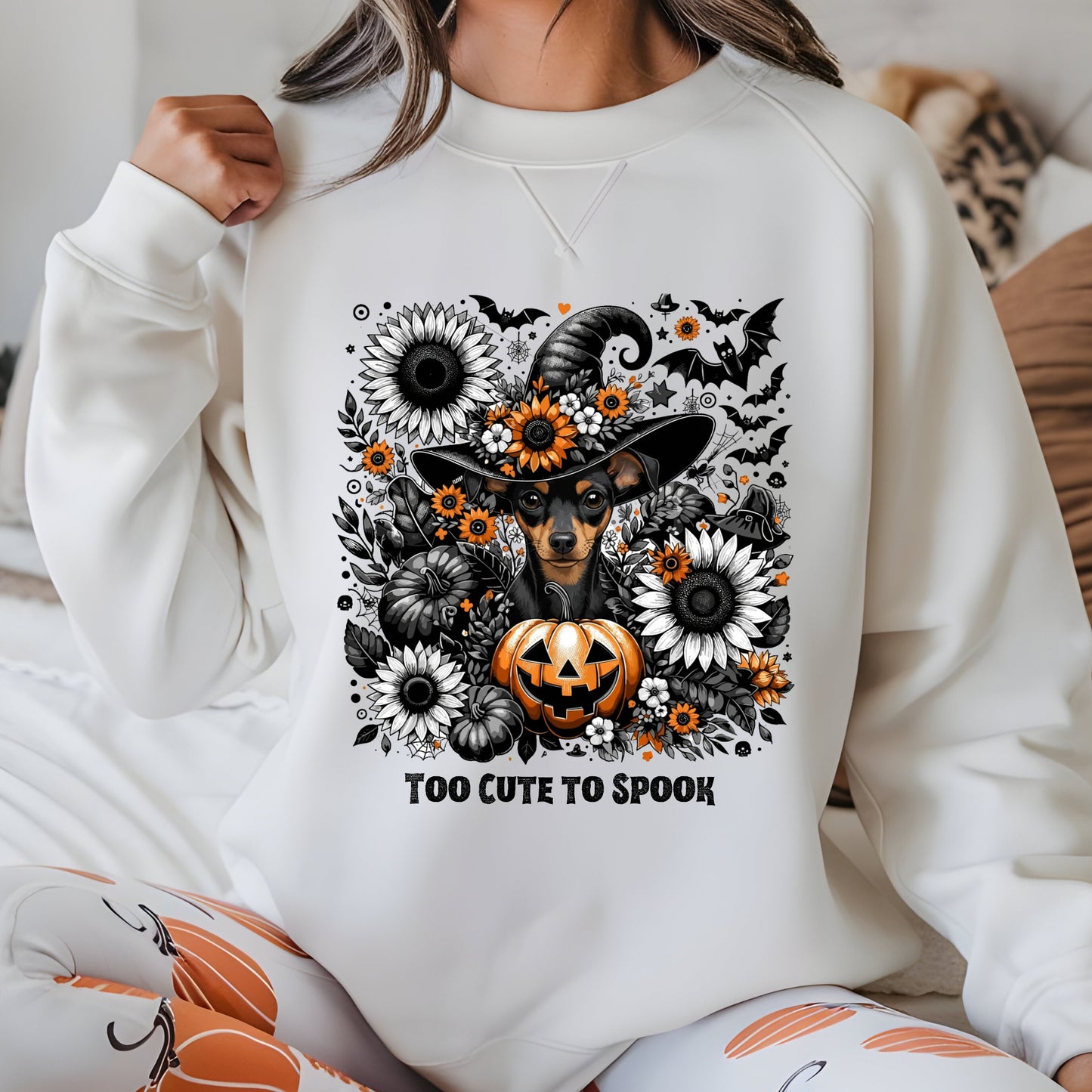 Person wearing a white sweatshirt with a Halloween-themed design featuring a dog in a witch hat, pumpkin, and flowers.