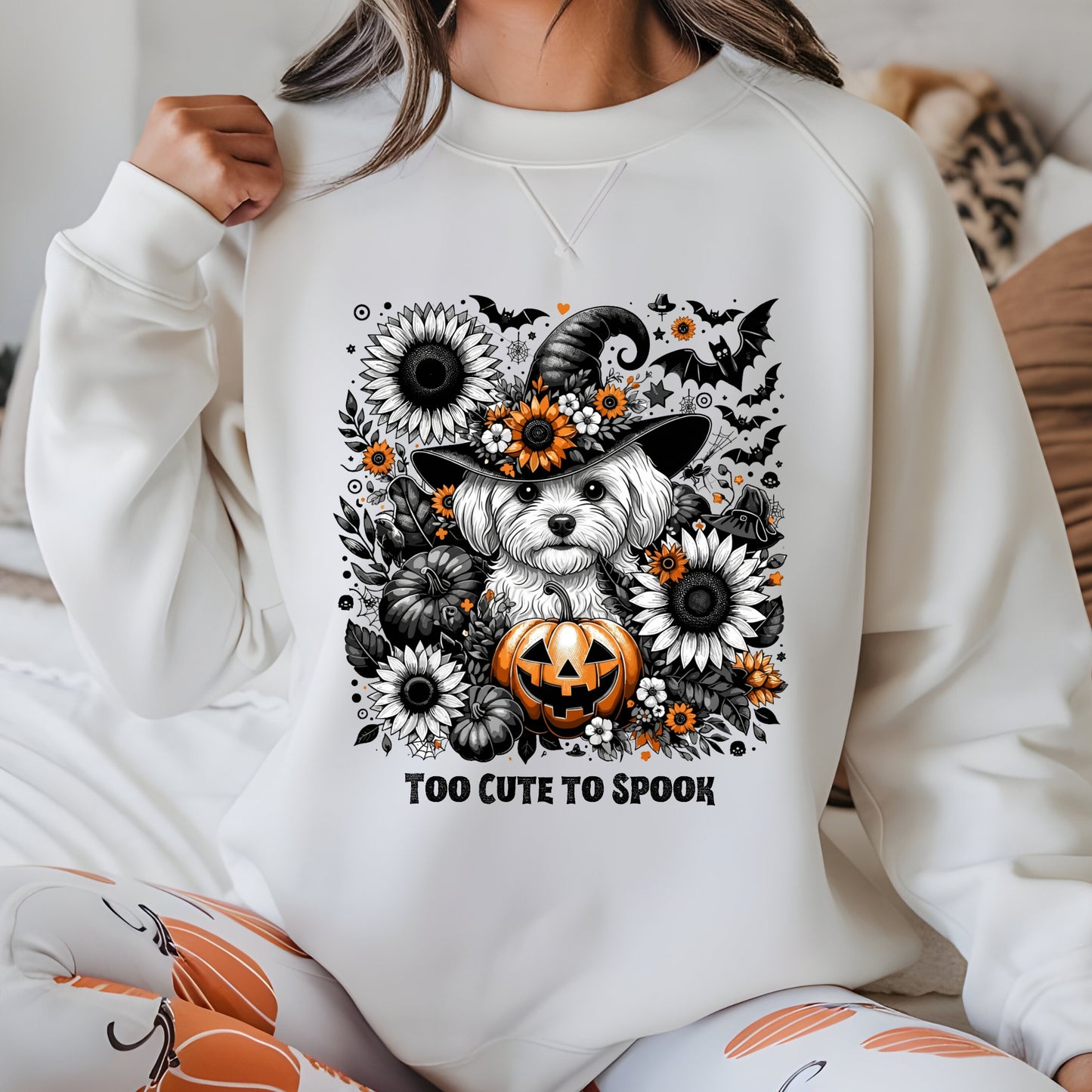 Person wearing a white sweatshirt with a Halloween-themed design featuring a dog in a witch hat and pumpkin.