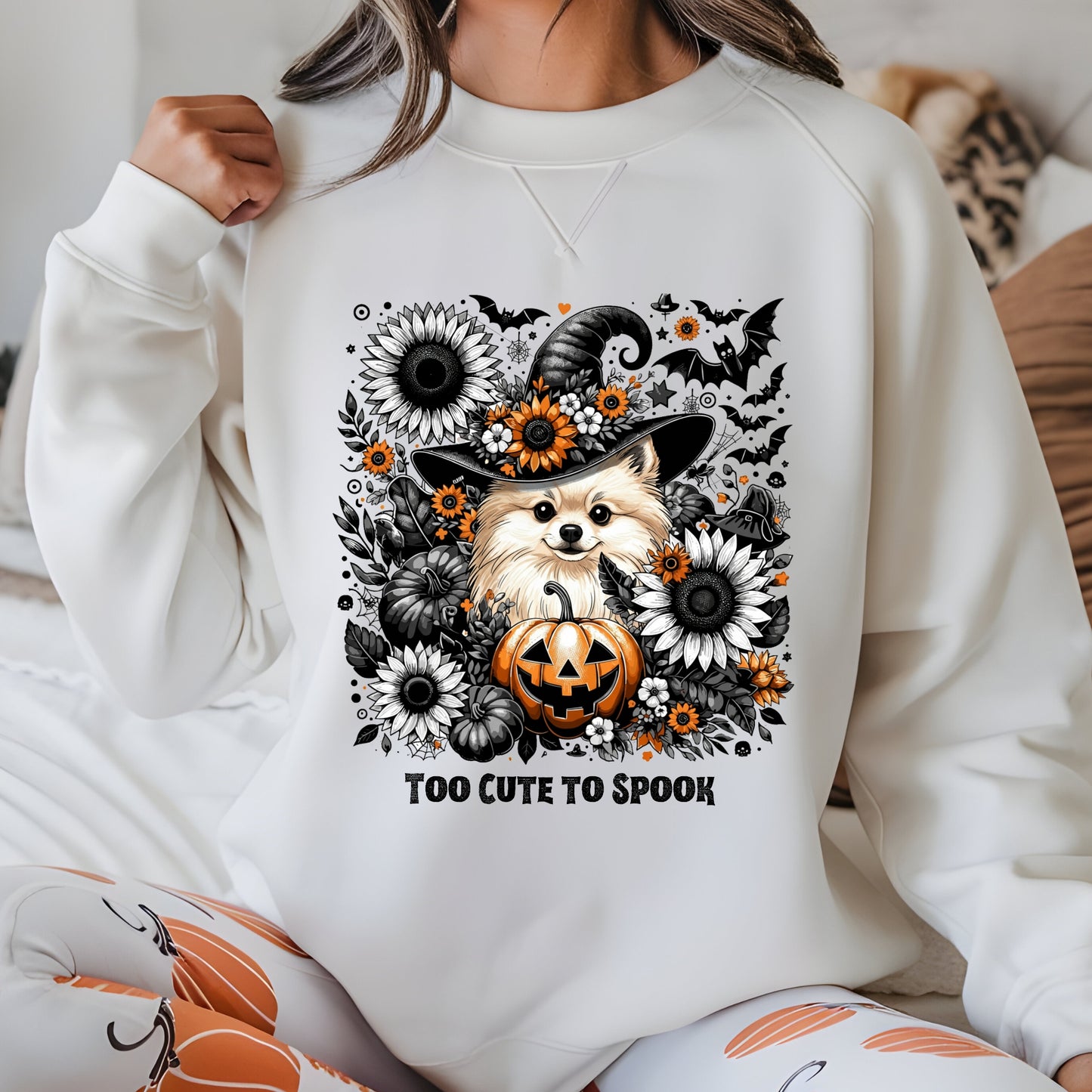 Person wearing a white sweatshirt with a Halloween-themed design featuring a dog, pumpkin, and flowers.