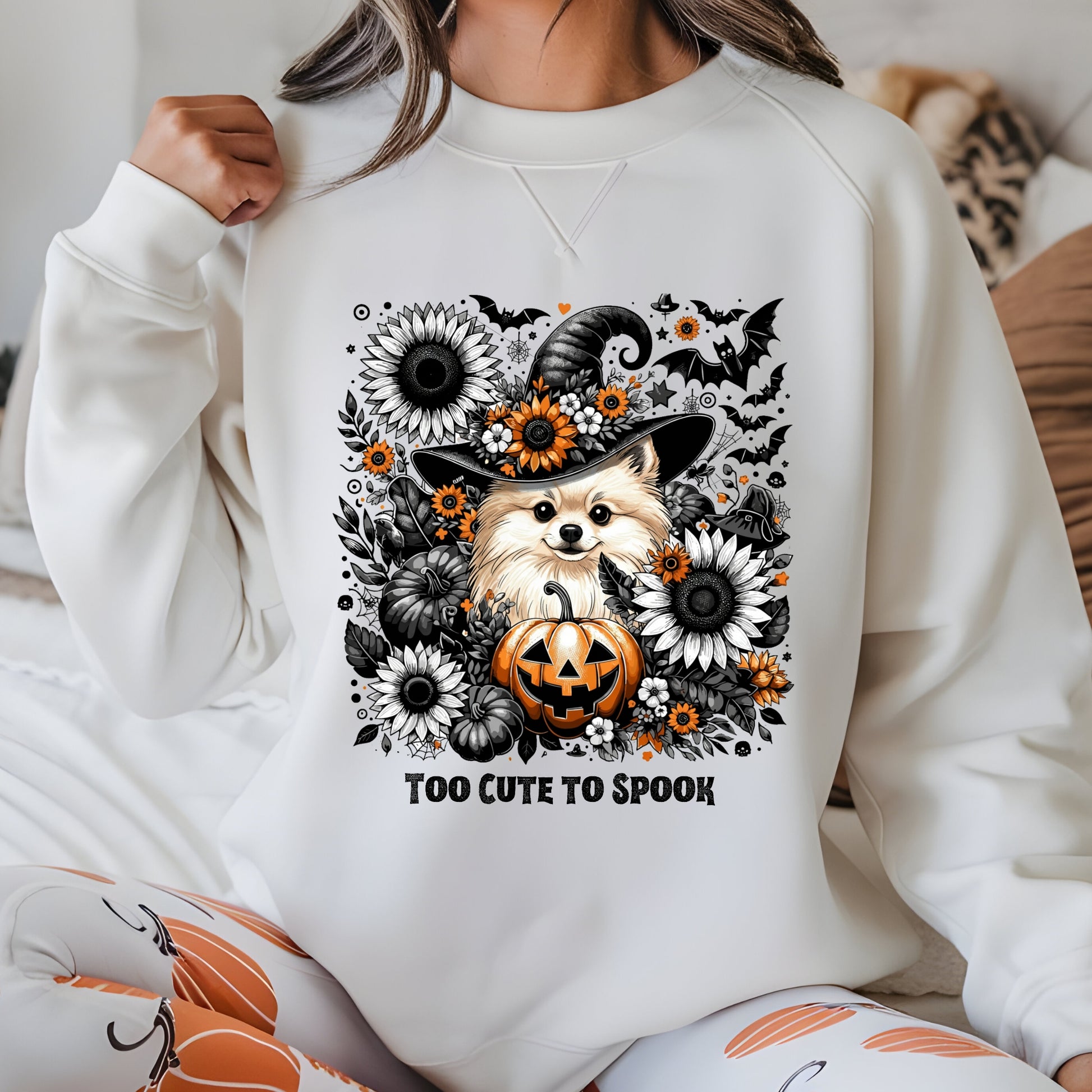 Person wearing a white sweatshirt with a Halloween-themed design featuring a dog, pumpkin, and flowers.