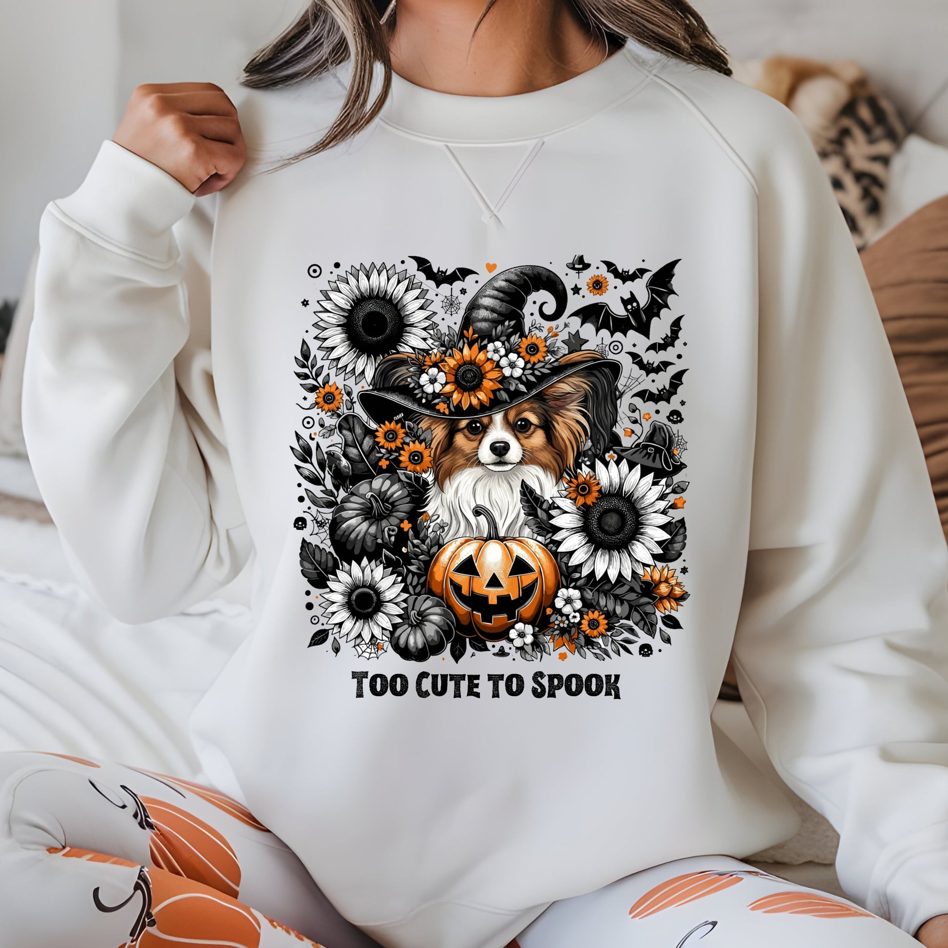 Person wearing a white sweatshirt with a Halloween-themed design featuring a dog, pumpkins, and flowers.