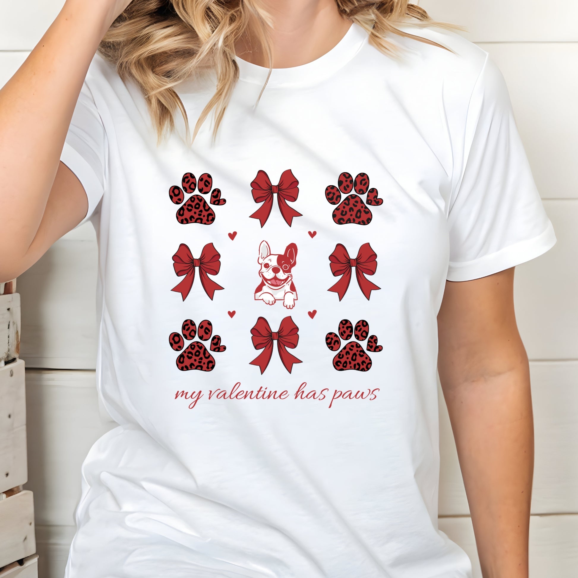 Whitet-shirt with red and black paw prints, bows, and a dog illustration on a white background.