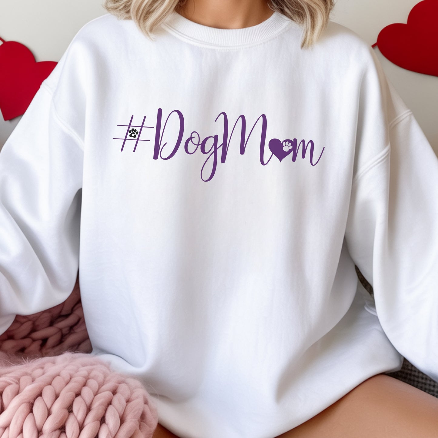 White sweatshirt with '#DogMom' text in purple on a person wearing it, with hearts in the background.
