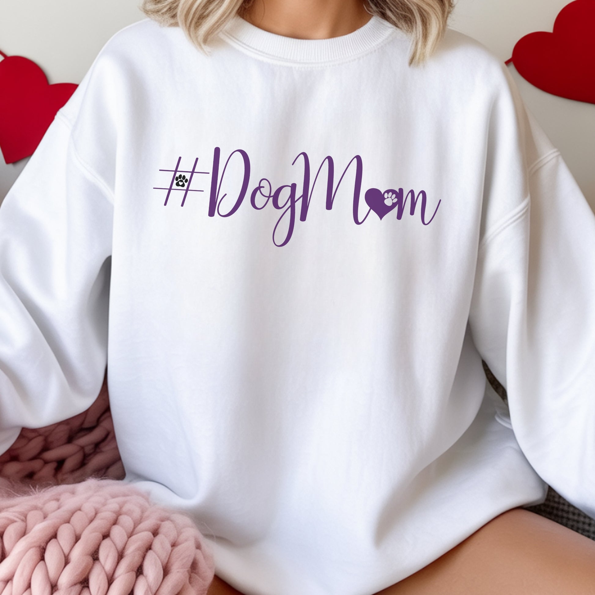 White sweatshirt with '#DogMom' text in purple on a person wearing it, with hearts in the background.