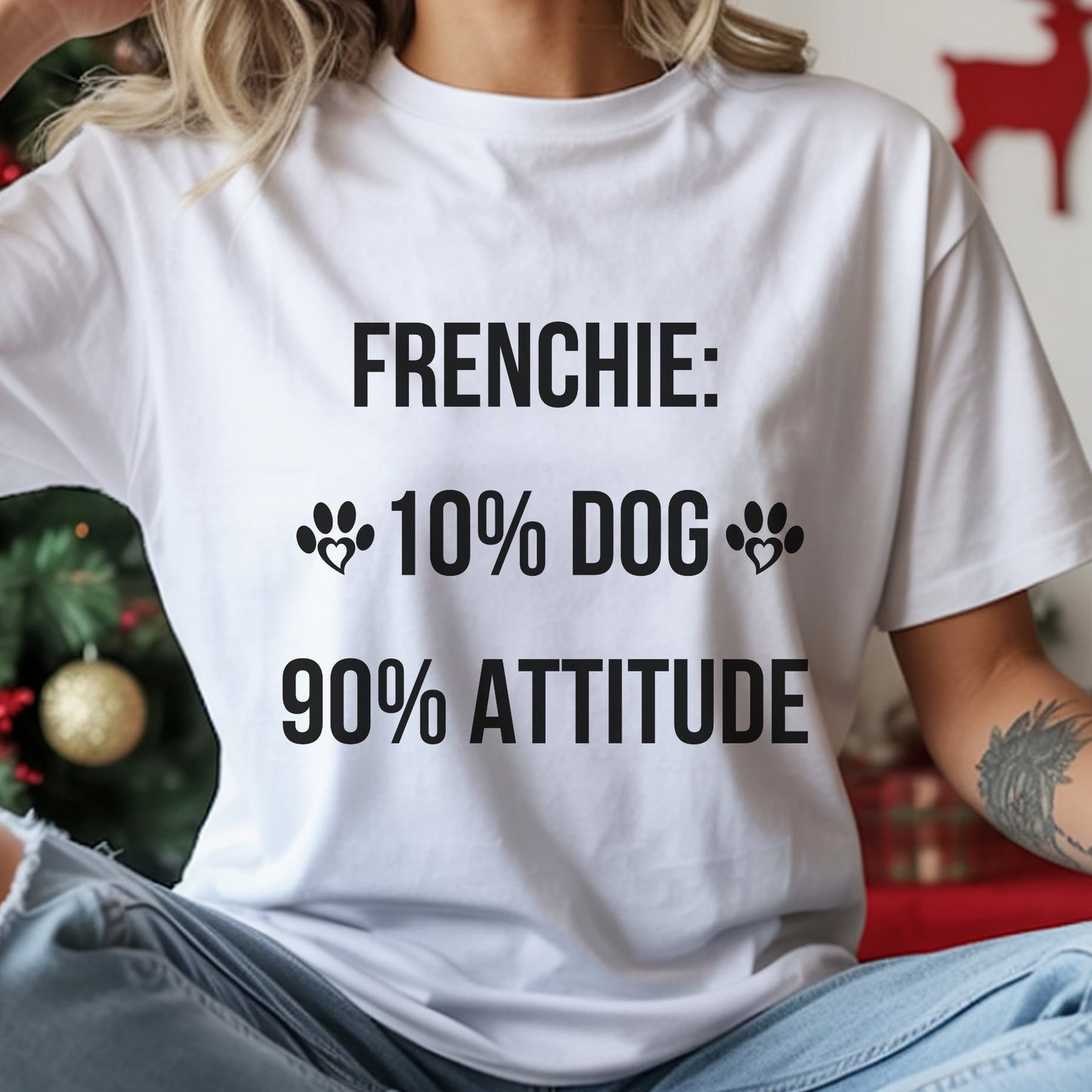 White t-shirt with text 'FRENCHIE: 10% DOG 90% ATTITUDE' worn by a person, with a festive background.
