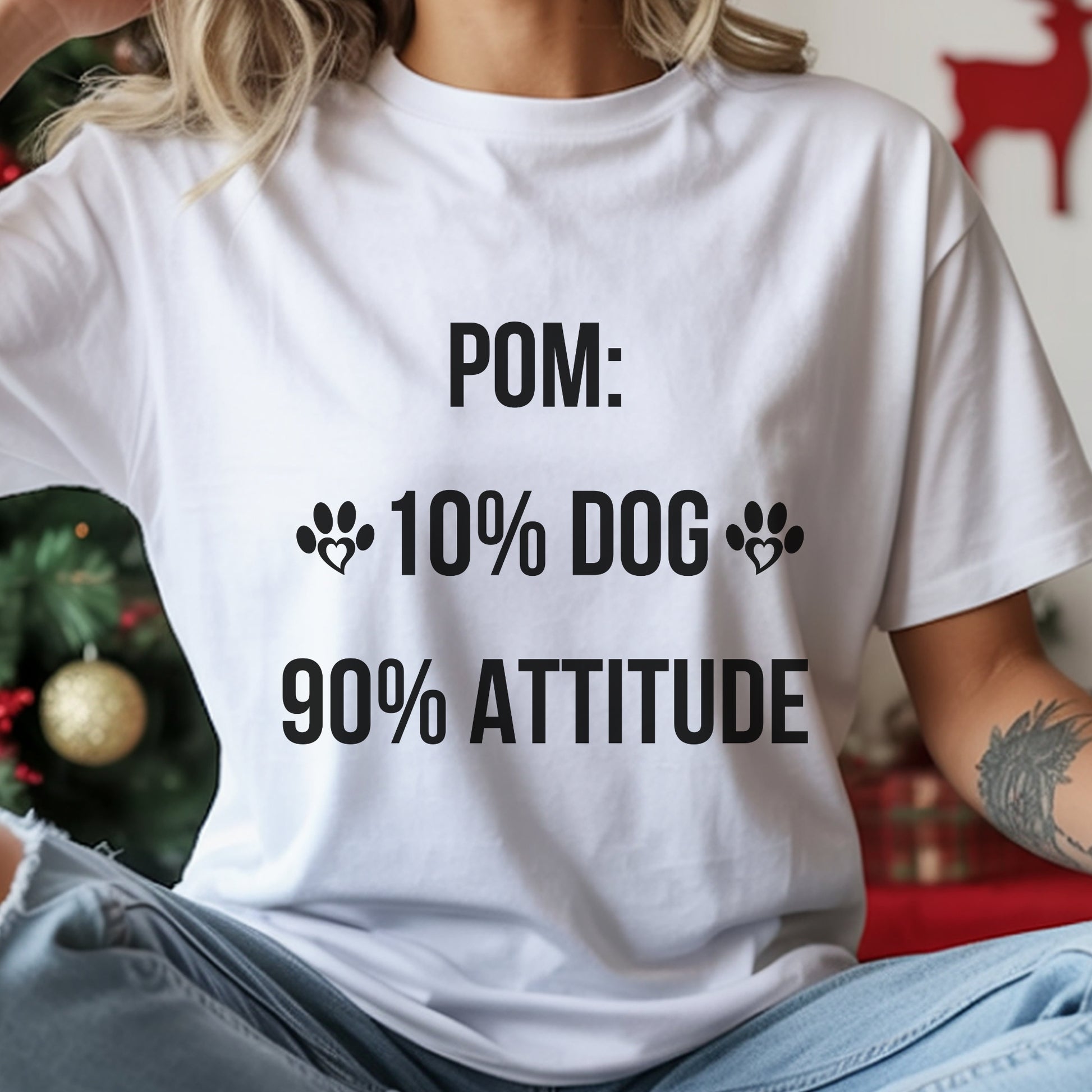 Person wearing a white t-shirt with humorous text design in front of a Christmas tree.