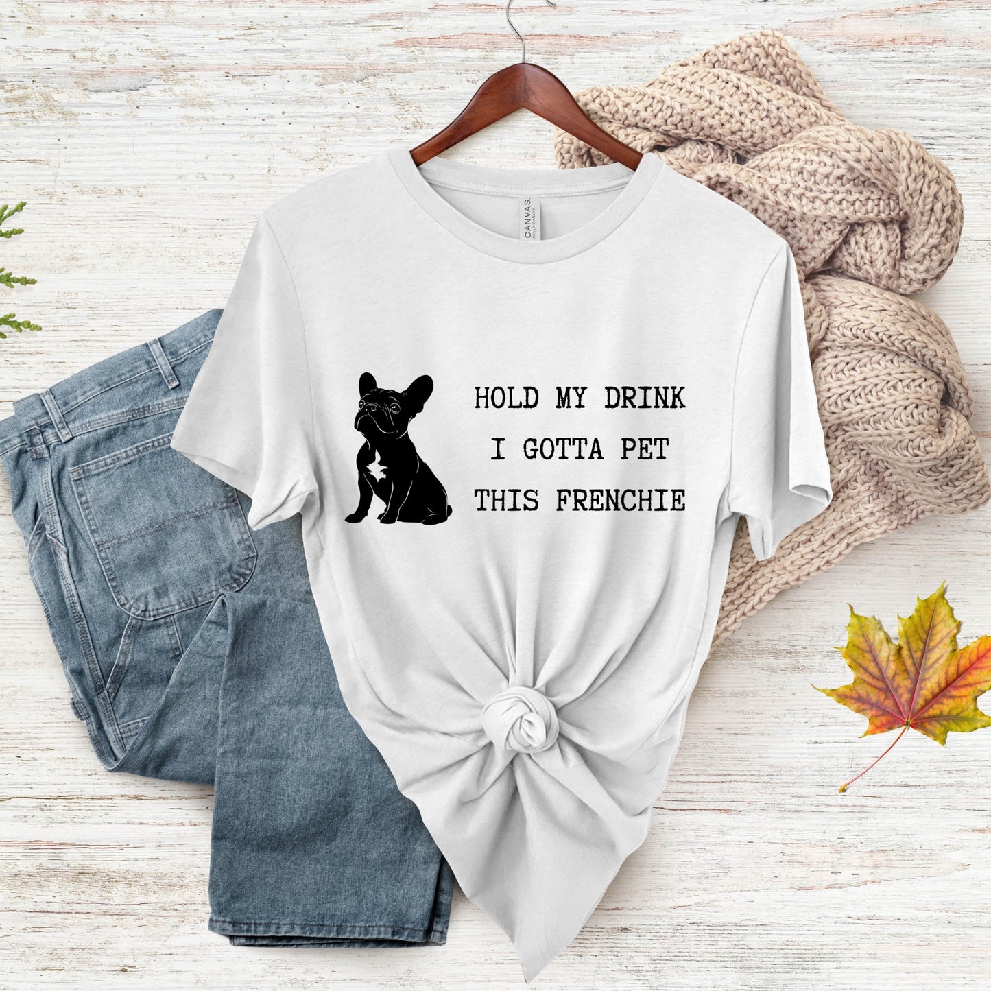 White t-shirt with a black dog graphic and text, paired with denim shorts on a wooden surface.