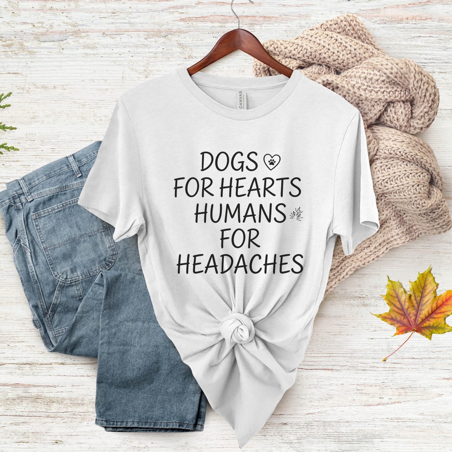 White t-shirt with text 'DOGS FOR HEARTS HUMANS FOR HEADACHES' on a wooden surface with jeans and a sweater.