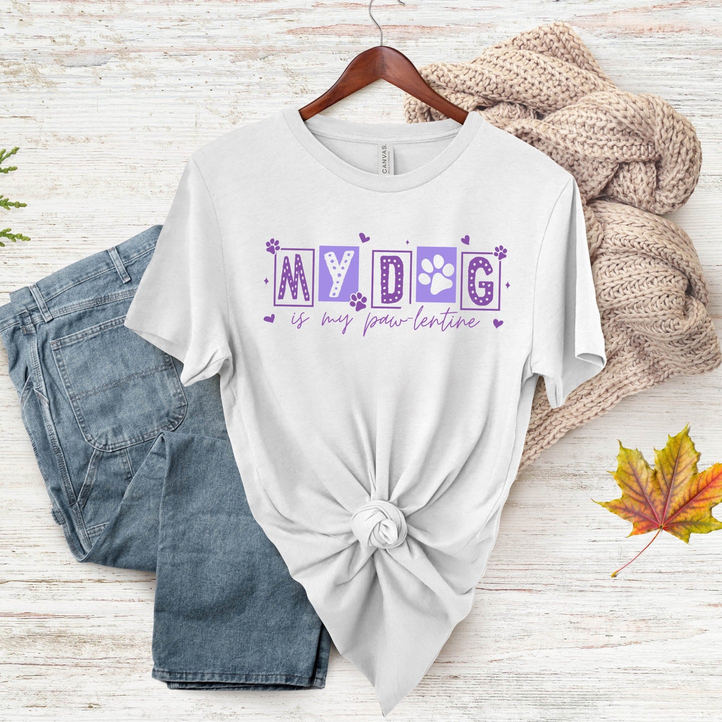 White t-shirt with 'MY DOG is my lover-tenant' text on a wooden surface with jeans and a sweater.