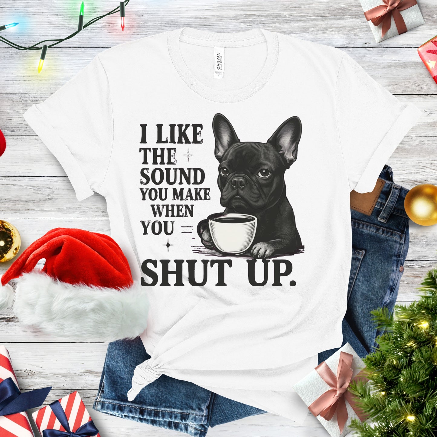 White t-shirt with a graphic of a dog holding a coffee cup and text, placed on a festive background with Christmas decorations.