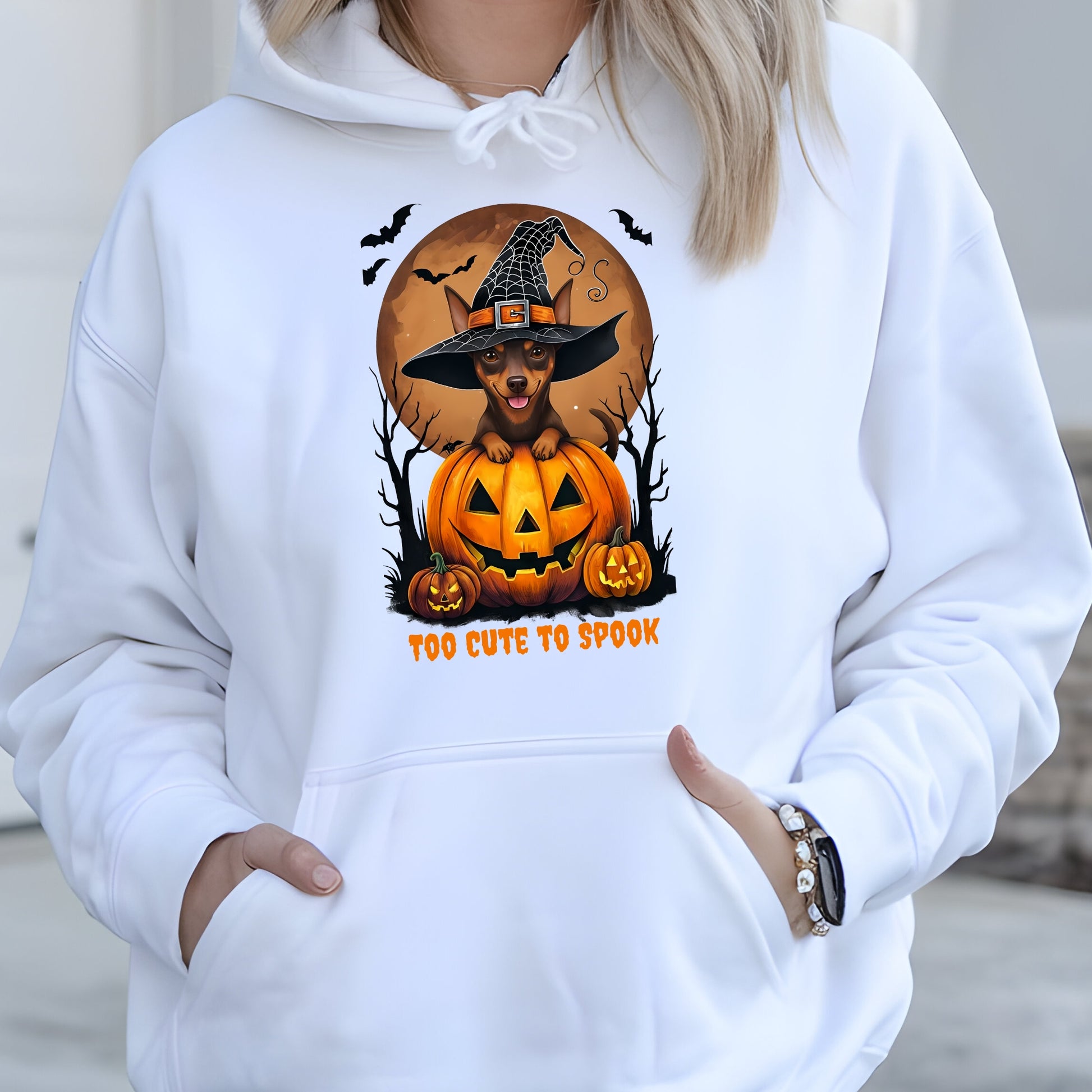 White hoodie with a Halloween-themed design featuring a dog in a witch hat on a pumpkin.