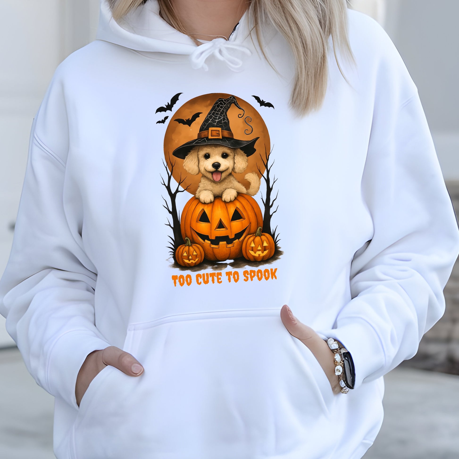 White hoodie with Halloween design featuring a dog in a pumpkin and text 'Too Cute to Spook'.