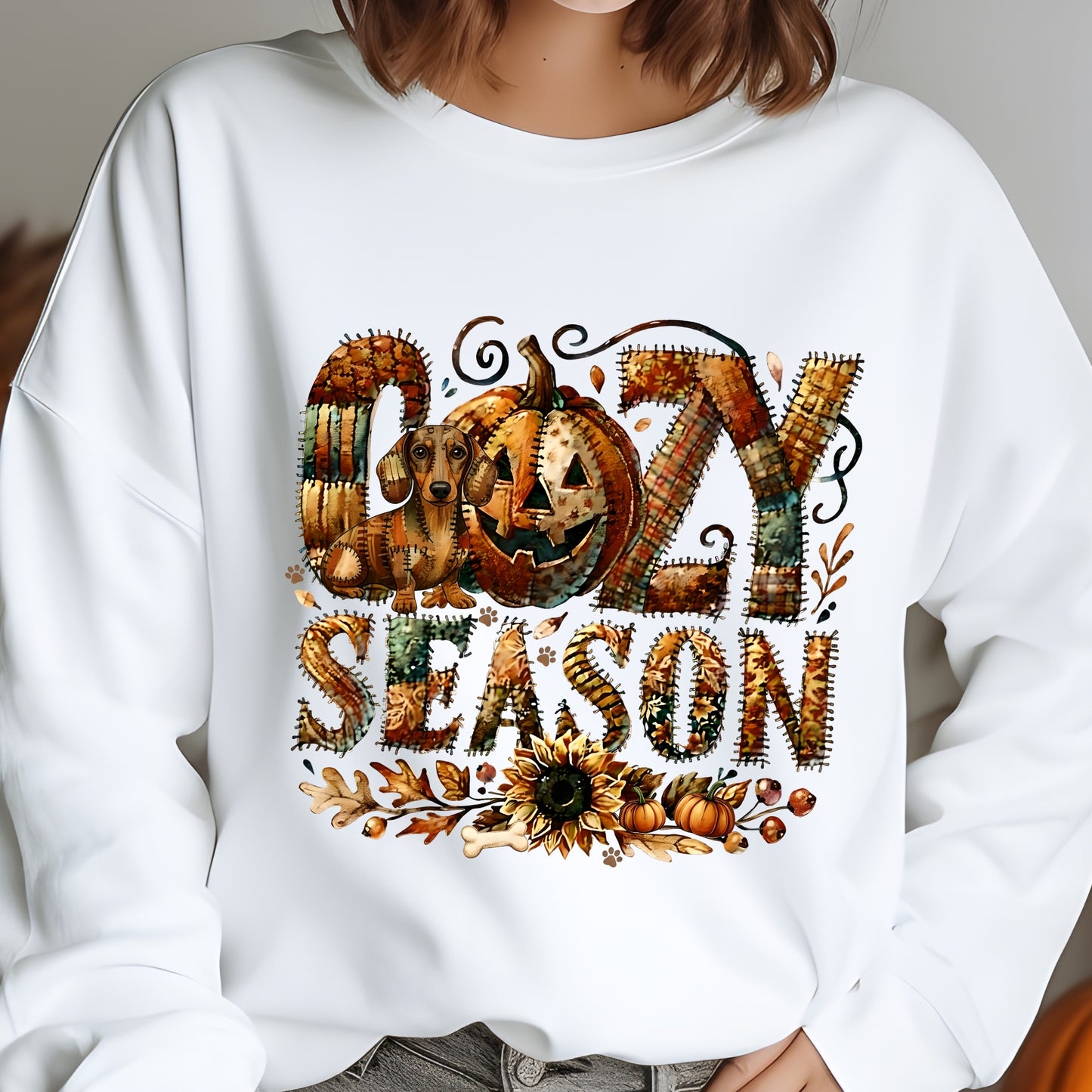 Cozy Season patchwork sweatshirt featuring a hidden Dachshound in autumn colors, surrounded by pumpkins, leaves, and a sunflower.Cozy patchwork sweatshirt with "Cozy Season" text, autumn colors, pumpkins, sunflower, and a hidden Dachshound motif.
