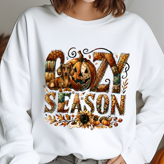 Cozy Season patchwork sweatshirt featuring a hidden Dachshound in autumn colors, surrounded by pumpkins, leaves, and a sunflower.Cozy patchwork sweatshirt with "Cozy Season" text, autumn colors, pumpkins, sunflower, and a hidden Dachshound motif.