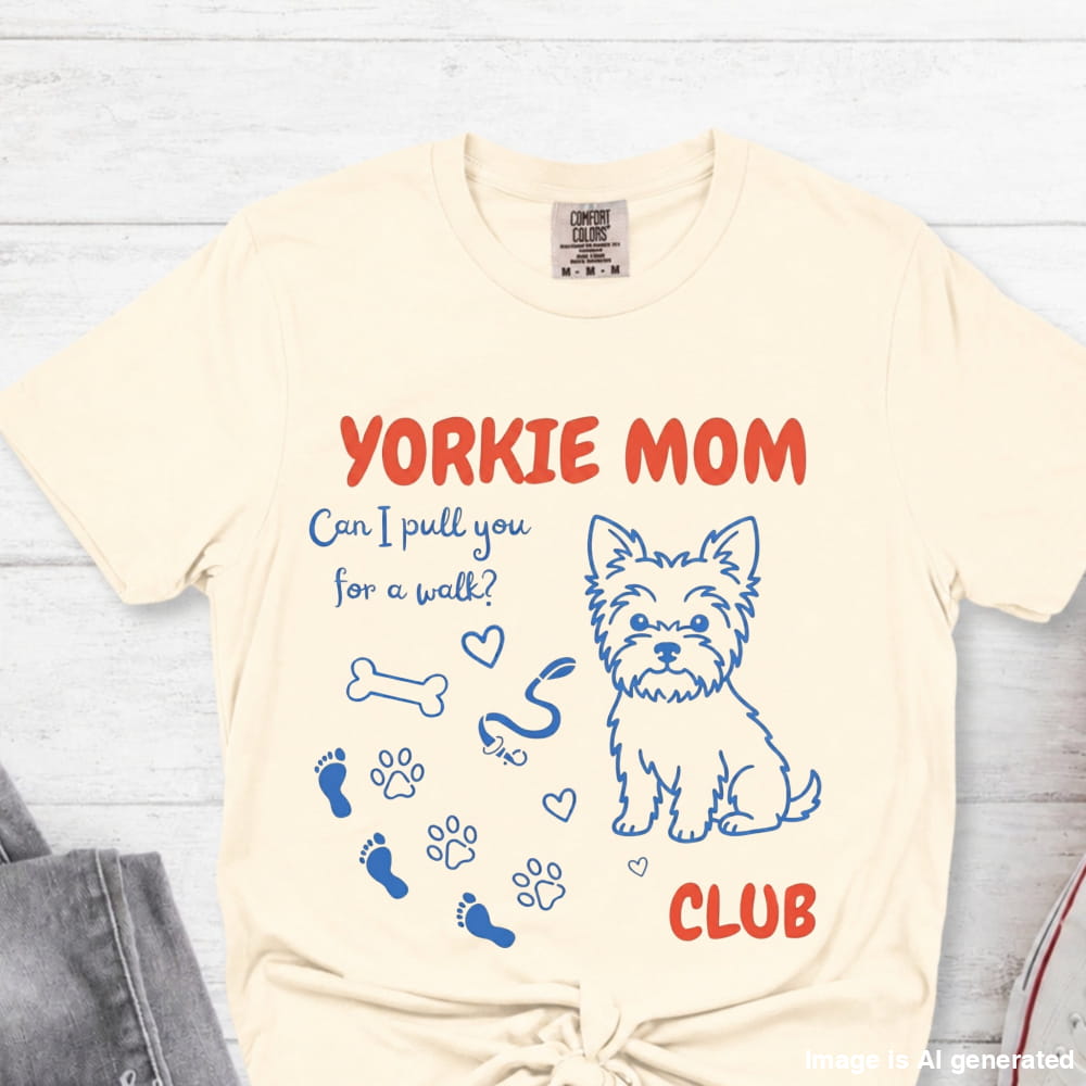 Beige t-shirt with Yorkie Mom graphic and text on a light wooden surface